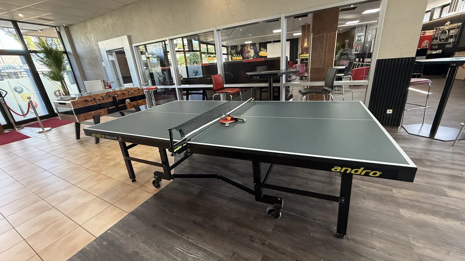 Tischtennisplatte in voller Größe im Saal von Billard Voerde, dahinter Kicker und Sitzplätze